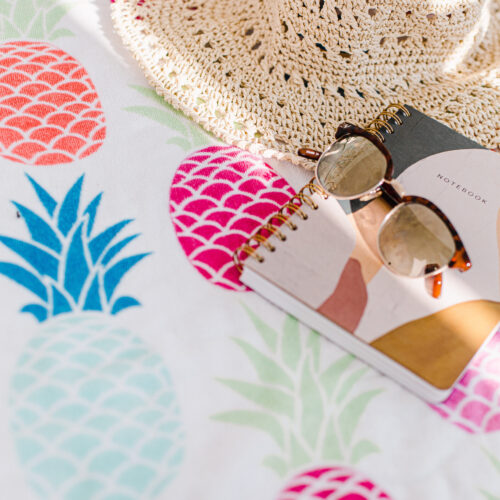 notebook-sunhat-and-sunglasses-on-pineapple-table-cloth